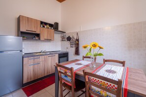 A kitchen with wooden cabinets, a refrigerator, and a dining table with a patterned tablecloth.