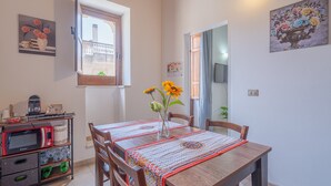 Zona pranzo con tavolo, sedie, un vaso con fiori, un forno a microonde e uno scaffale con oggetti da cucina.