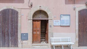 L'ingresso di un edificio con una porta in legno, una panchina e un cartello.