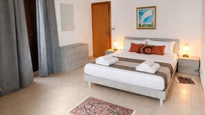Camera d'albergo con un letto, due comodini, una lampada da notte, una porta, una finestra con tende e un quadro appeso al muro.