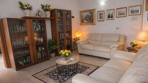 Un soggiorno con un divano, un tavolino con fiori, una libreria e una lampada.