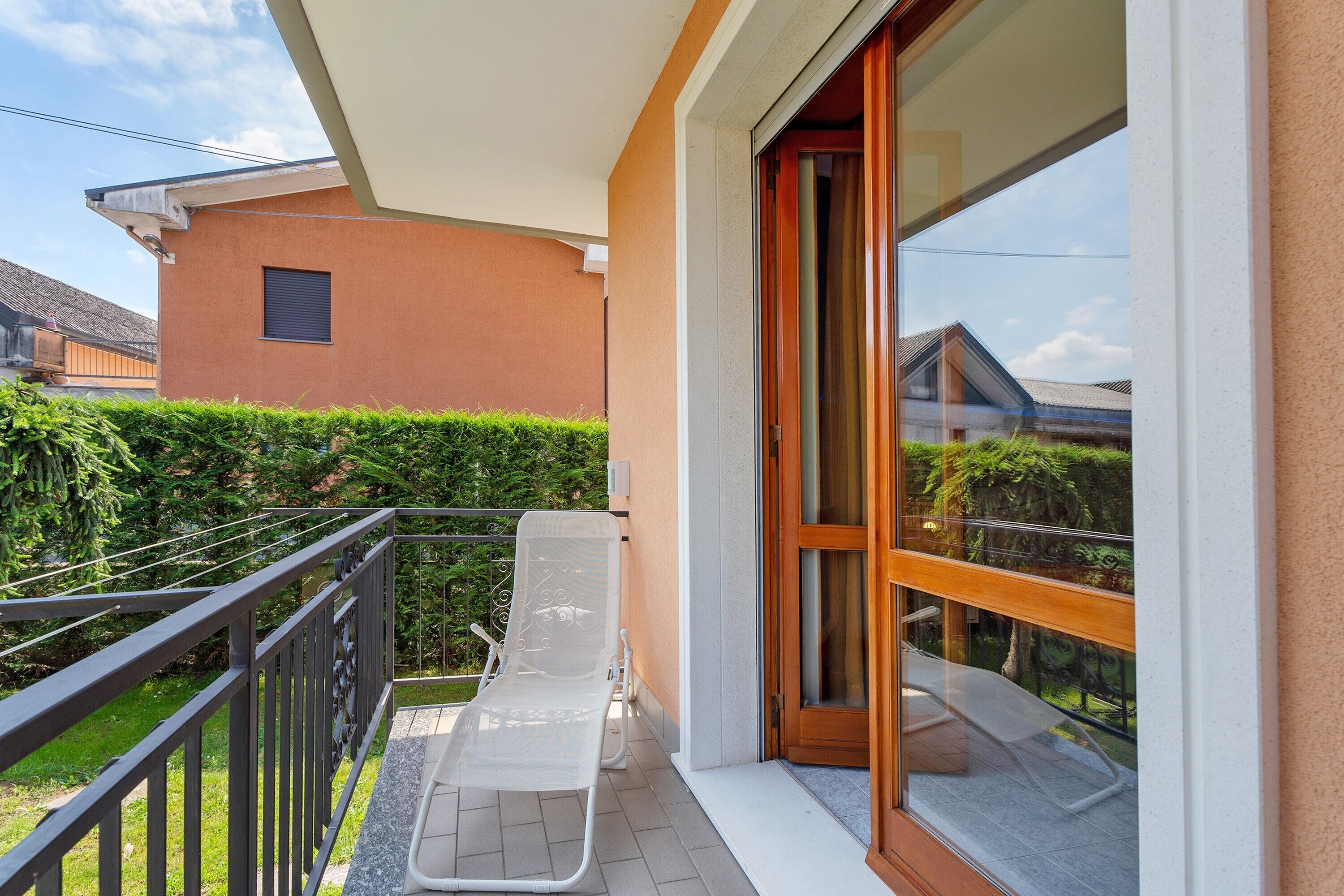 Een balkon met een witte stoel, een houten deur en uitzicht op een aangrenzend gebouw.