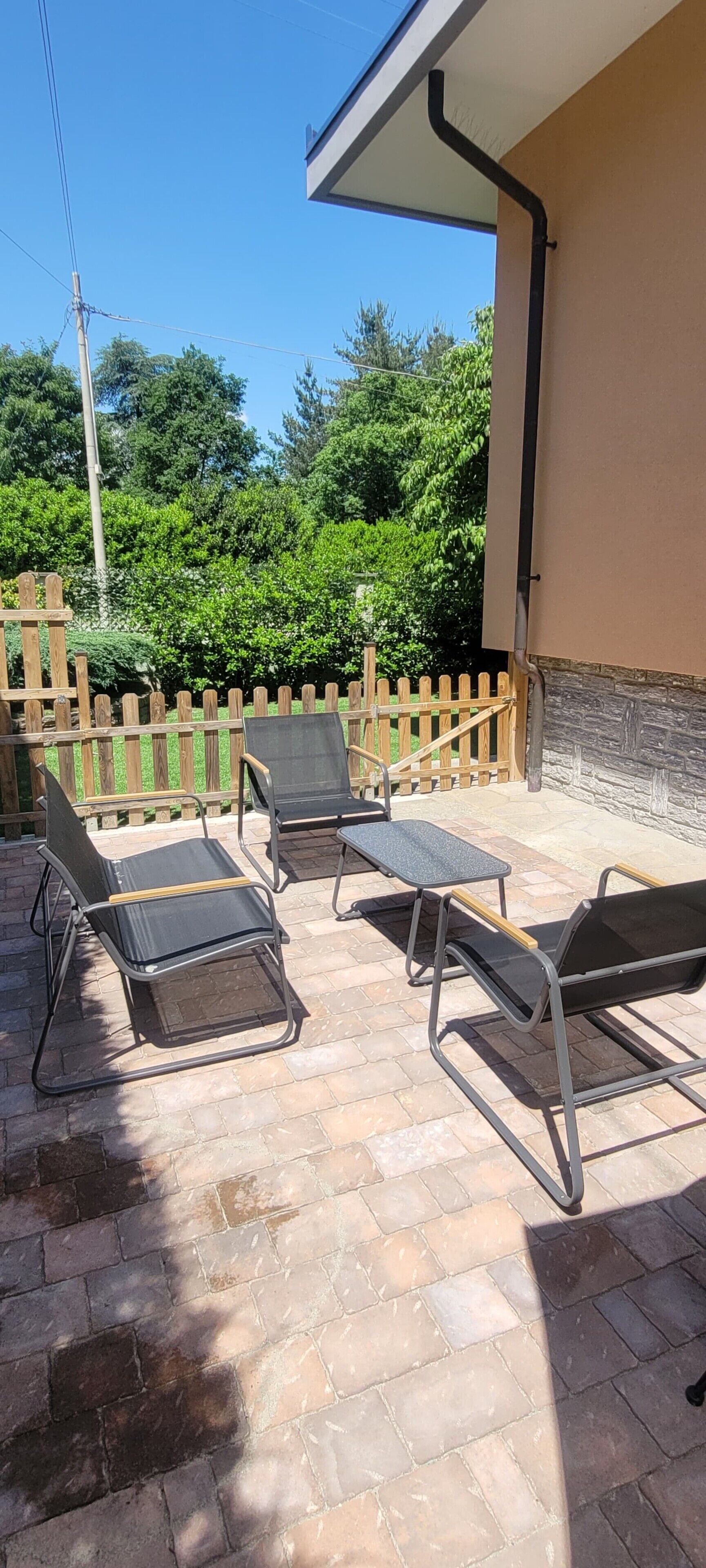 An outdoor patio with four metal chairs and a small table, surrounded by a wooden fence and greenery.