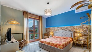 Un dormitorio con una cama grande, televisor, escritorio y pared de piedra.