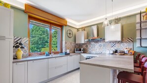 Una cocina moderna con armarios blancos, una isla grande, un ventanal con vistas y un reloj en la pared.