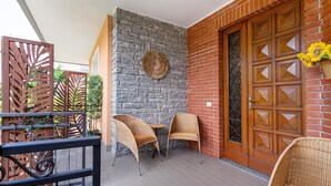 Un patio con sillas de mimbre, un muro de piedra y una puerta de madera con panel de vidrio.
