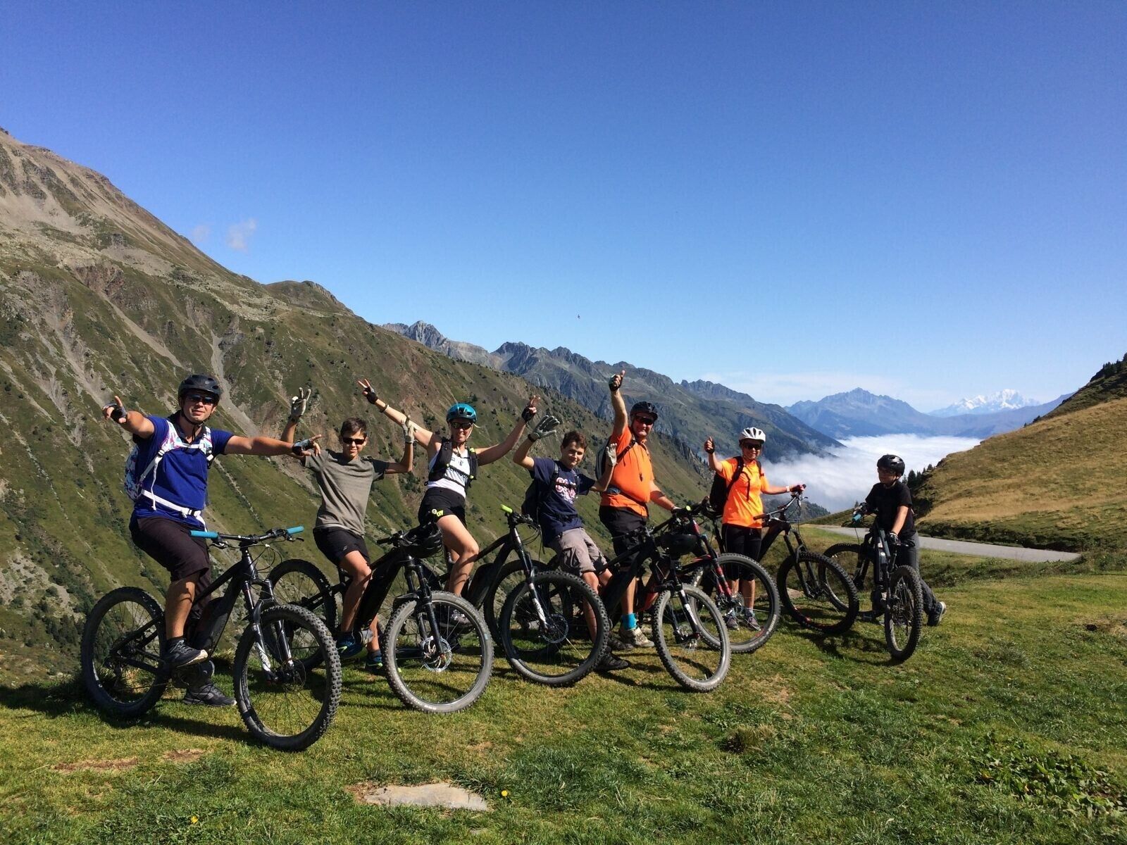 A group of cyclists on a mountain path with a clear sky and distant mountains.