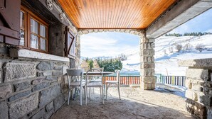 A stone building with a wooden roof, a table with chairs, and a view of a snowy landscape. - Apartment 'Chalet -Les Aiguilles- Rdc' with Mountain View, Terrace and Garden (Albiez-Montrond)