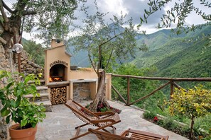 Une terrasse en pierre avec un poêle à bois, des sièges d’extérieur et une vue sur un paysage montagneux.