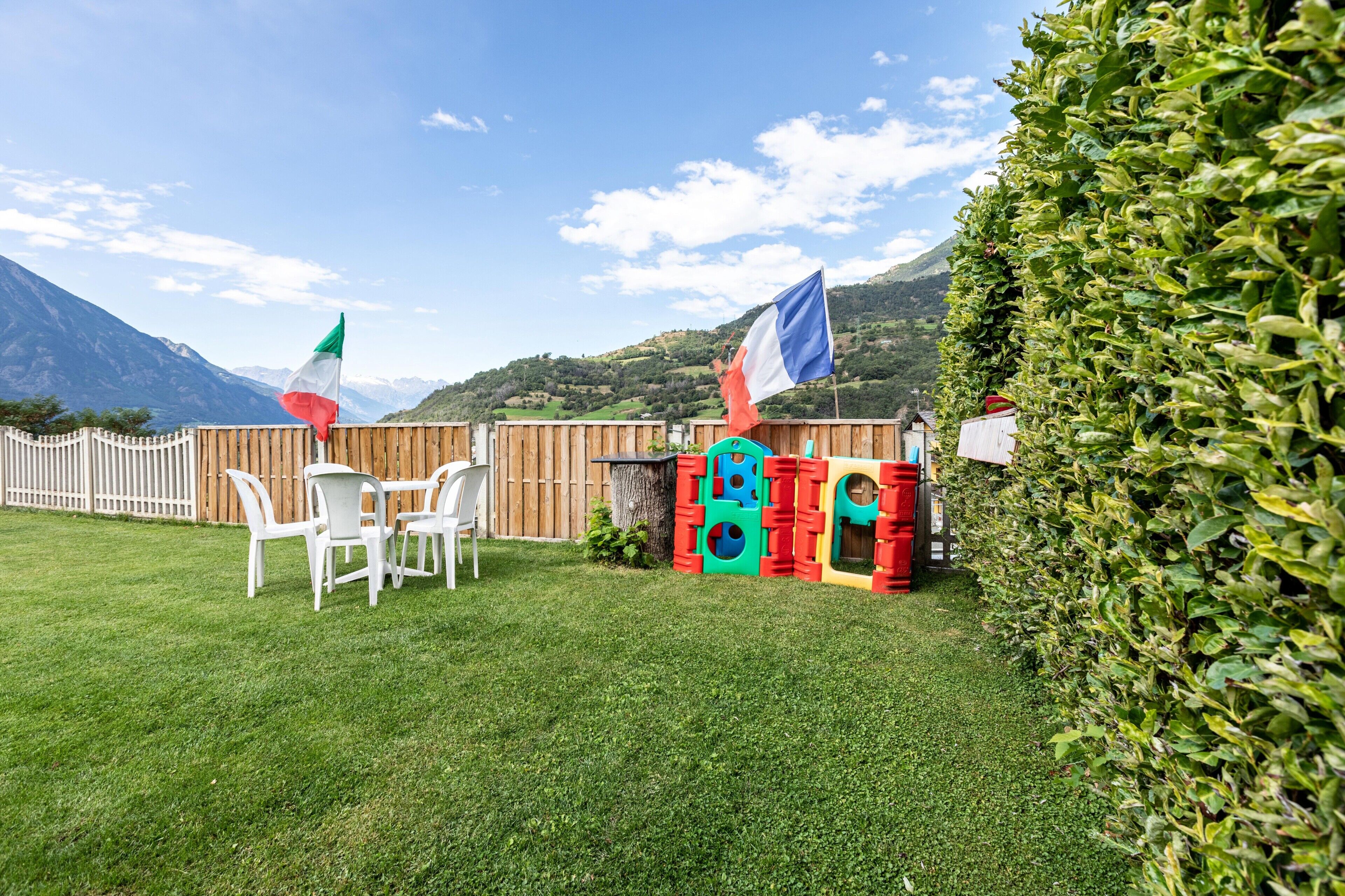 A grassy outdoor area with a wooden fence, a table with chairs, and colorful play structures.