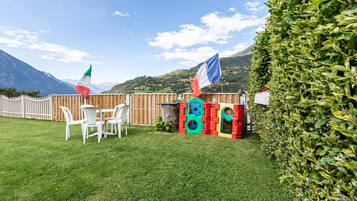 A grassy outdoor area with a wooden fence, a table with chairs, and colorful play structures.