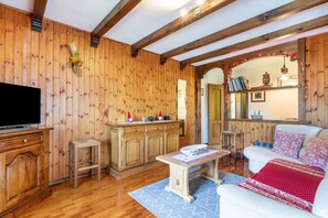 Une pièce aux murs lambrissés, équipée d’un téléviseur, de meubles en bois, d’un canapé blanc et d’une petite table.