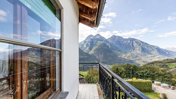 Ein Balkon mit Bergblick, einer Glastür und einem schwarzen Geländer.
