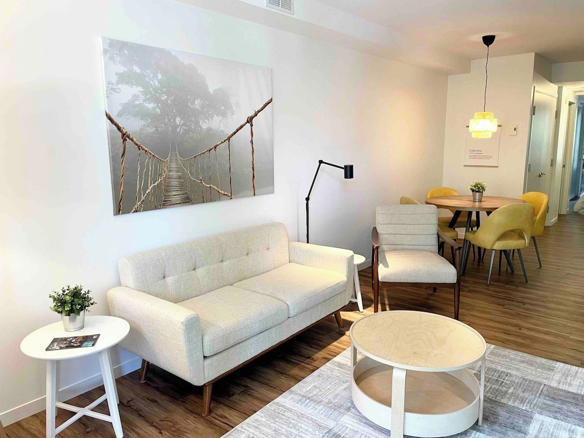 Uma sala de estar moderna com um sofá, uma mesa de centro e um espaço de jantar com cadeiras amarelas.
