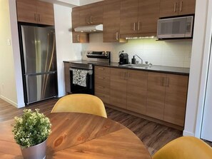 A modern kitchen with wooden cabinets, stainless steel appliances, and a dining area with a round table and yellow chairs. - A charming home on 3rd Avenue in Limoilou. (Québec)