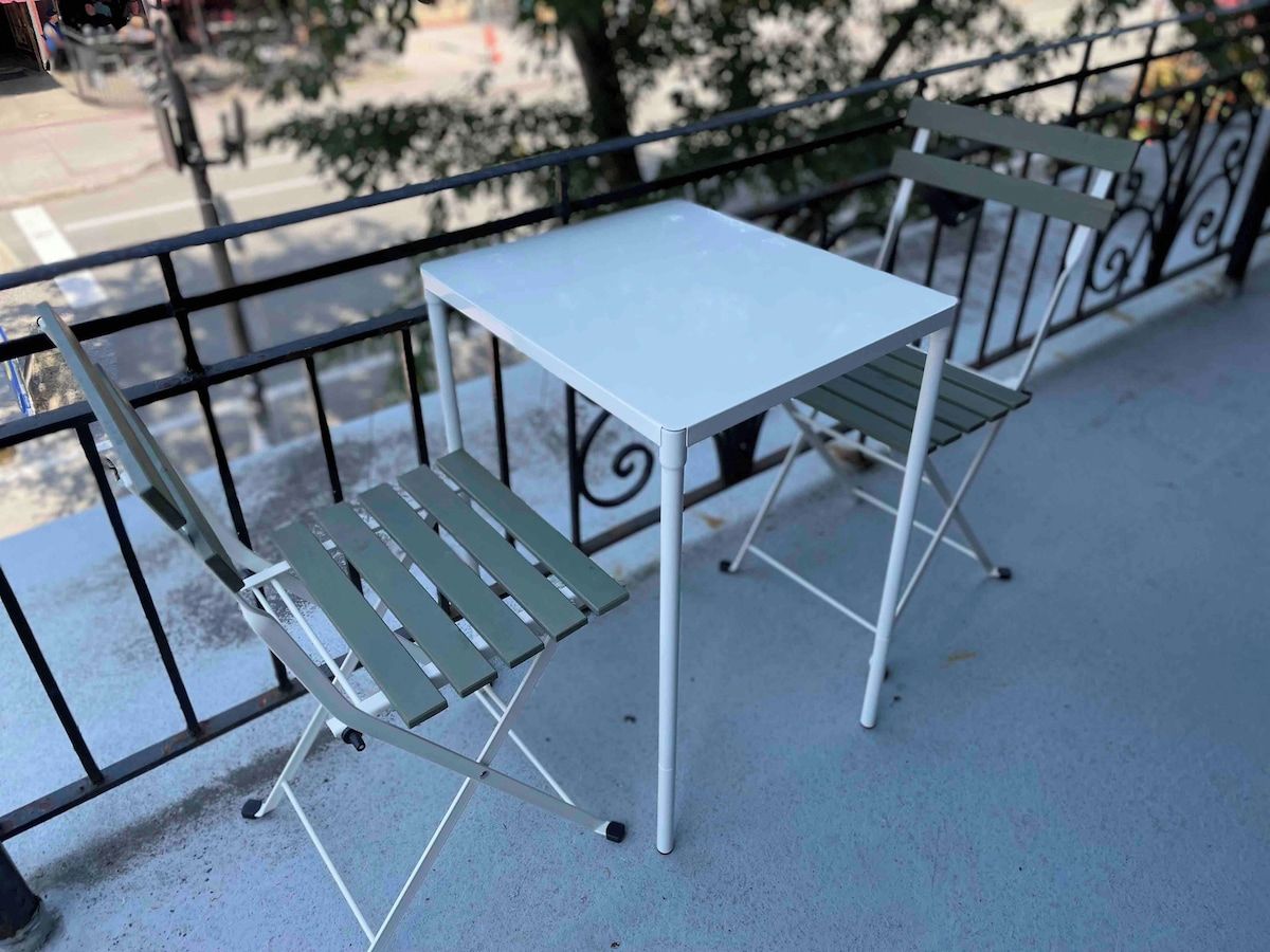 Une table à ossature métallique et deux chaises sur un balcon doté d’une rambarde en métal.
