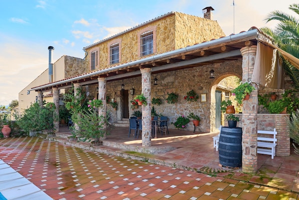A stone building with a covered patio, outdoor seating, and potted plants.