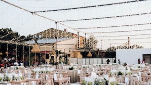 An outdoor event space with tables set for dining, string lights overhead, and a building in the background.