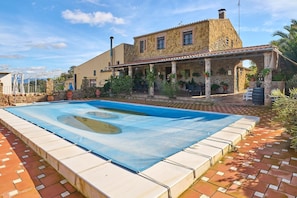 A stone building with a swimming pool, outdoor seating, and potted plants.