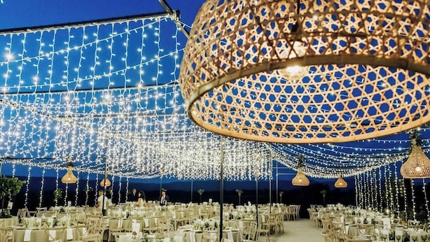 An indoor venue with tables set for dining, string lights overhead, and a large decorative lamp.