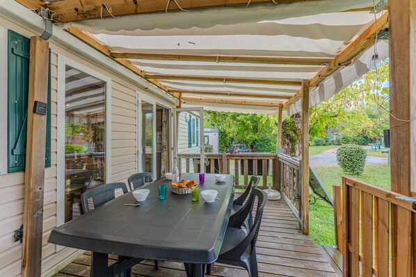 Un patio techado con una mesa lista para comer, asientos exteriores y vistas al jardín trasero.