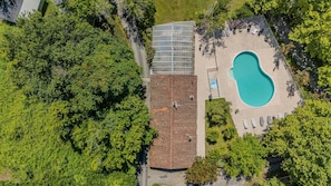 Vista aérea de una propiedad con piscina, un patio cubierto y abundante vegetación que rodea el terreno.