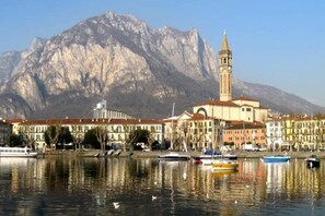 Vista al frente del agua con un edificio destacado que incluye una torre, barcos amarrados en la orilla y una montaña al fondo.