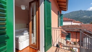 Un balcón con cama, contraventanas verdes y vistas a la montaña.
