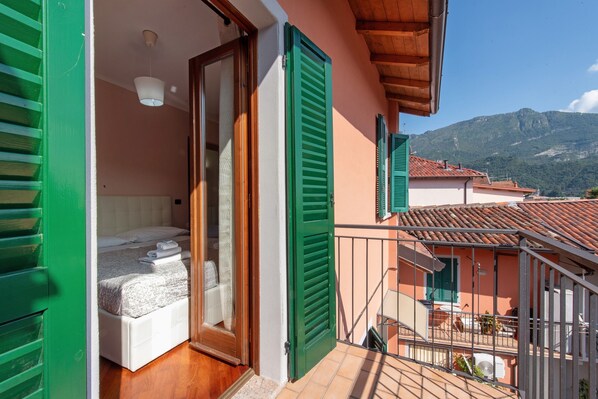 Un balcón con cama, contraventanas verdes y vistas a la montaña.
