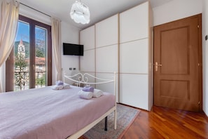 Une chambre à coucher avec un lit, un téléviseur fixé au mur, une porte en bois et une fenêtre avec des rideaux.
