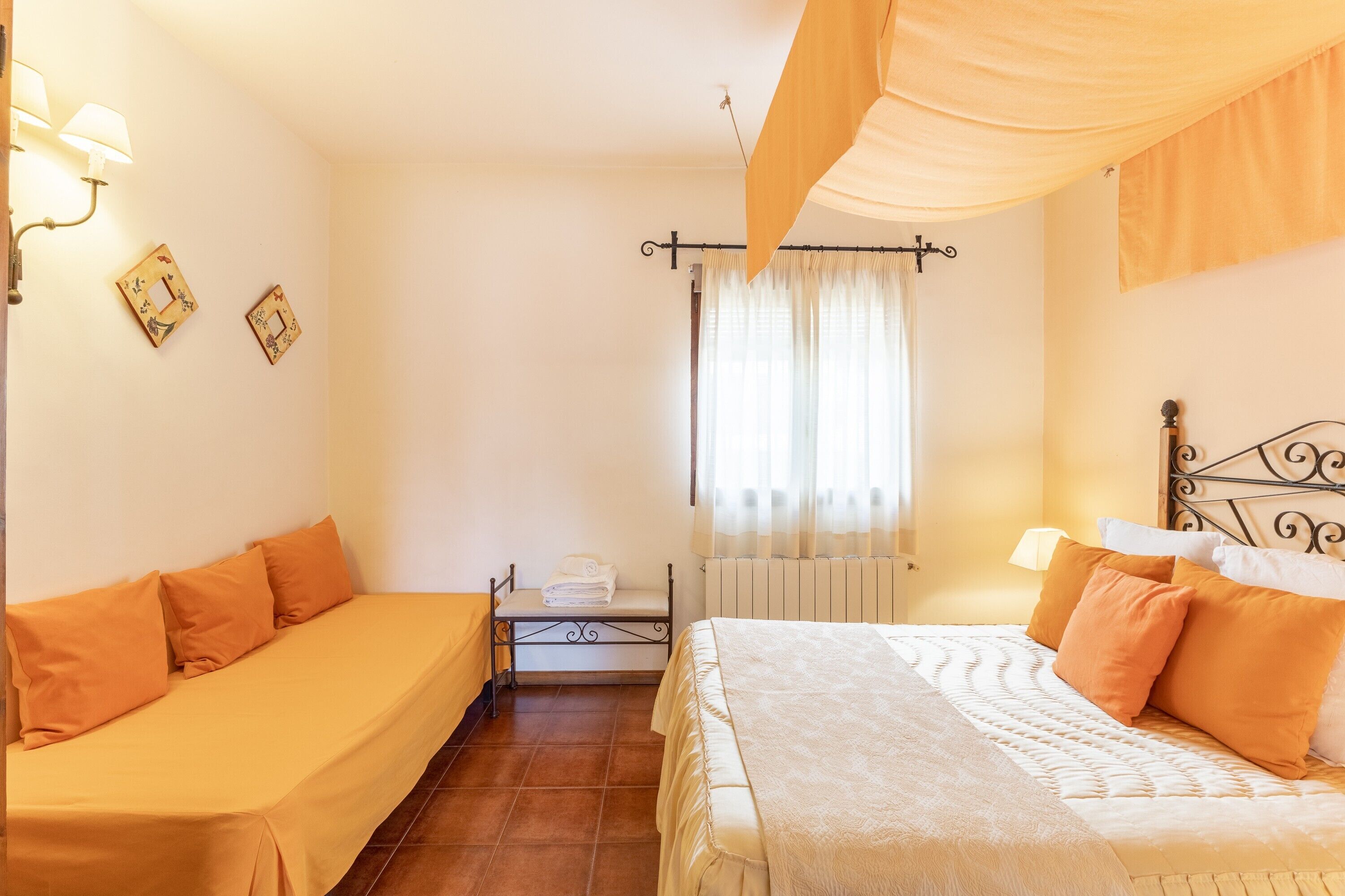 A bedroom with two beds, a radiator, a window with curtains, and wall-mounted lamps.