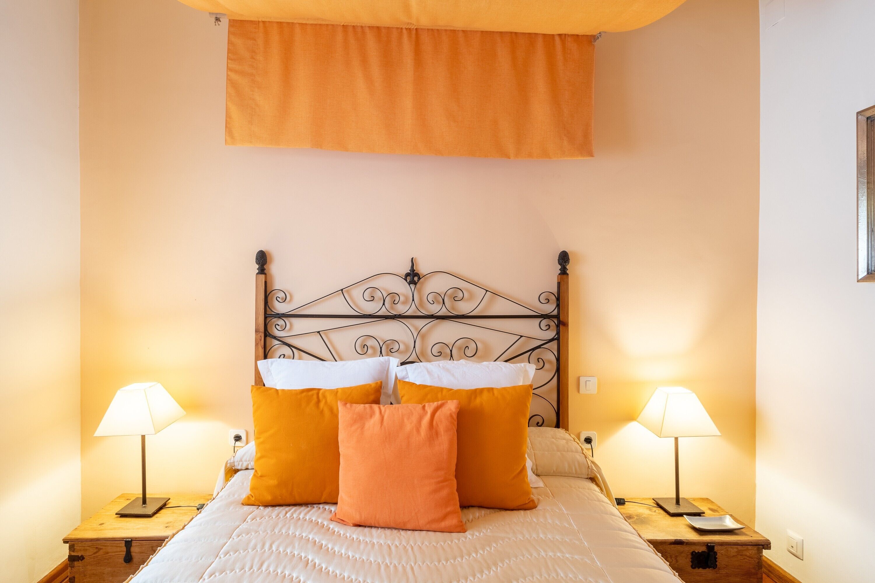 A neatly made bed with a headboard, two bedside lamps, and a wooden nightstand with a lamp.