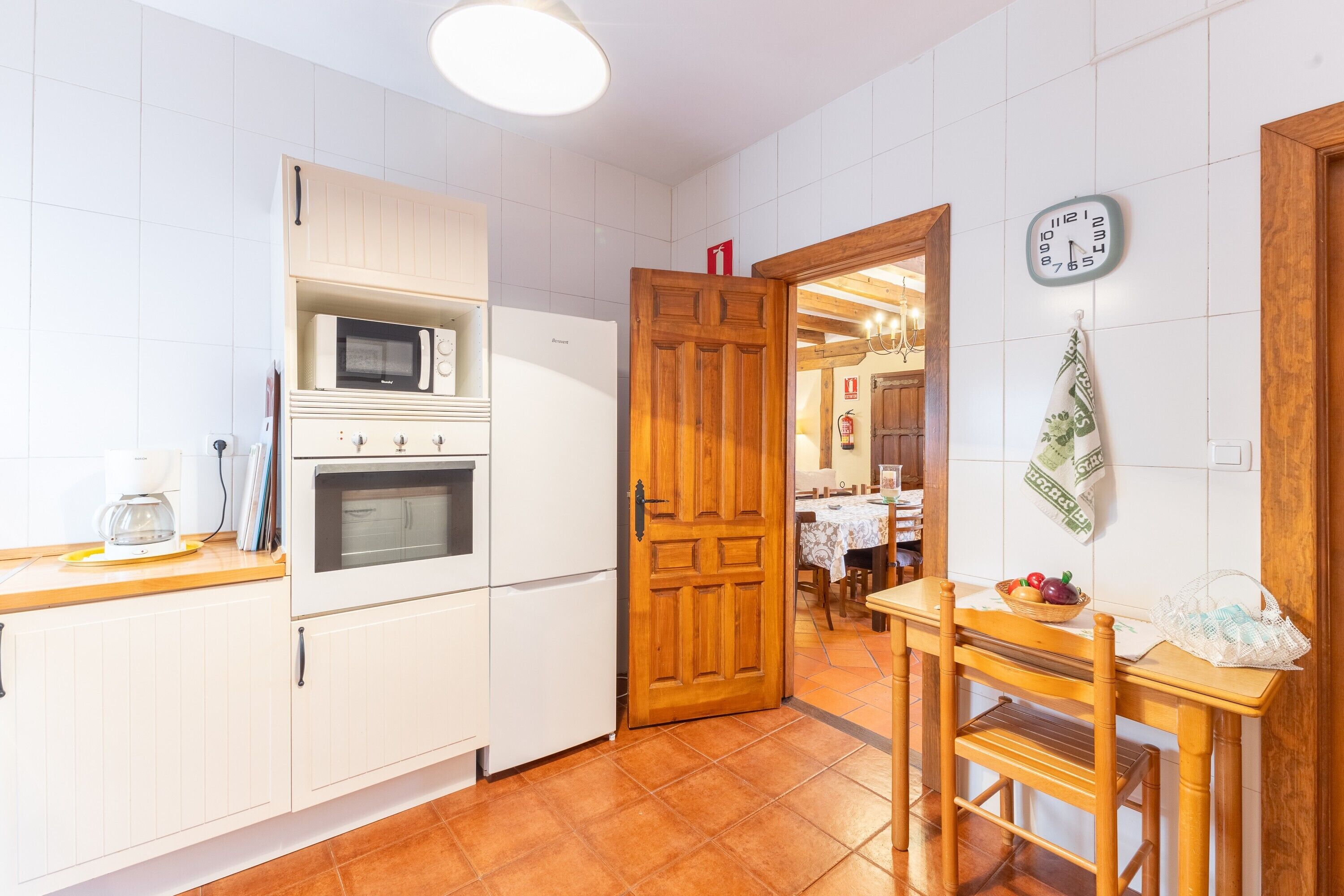 Eine Küche mit weißen Schränken, einer Mikrowelle, einem Backofen und einer Holztür, die in einen Essbereich führt.