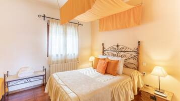 A bedroom with a bed, bedside tables, a bench, and a window with curtains.