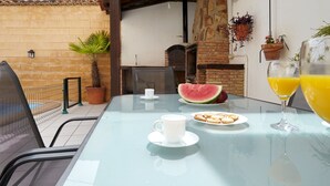 A glass table with a white cup, a plate with food, a glass of orange juice, and a watermelon slice.