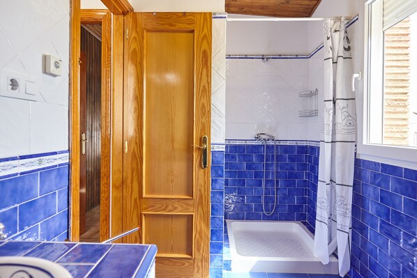 A bathroom with a wooden door, a shower with blue tiles, and a window.