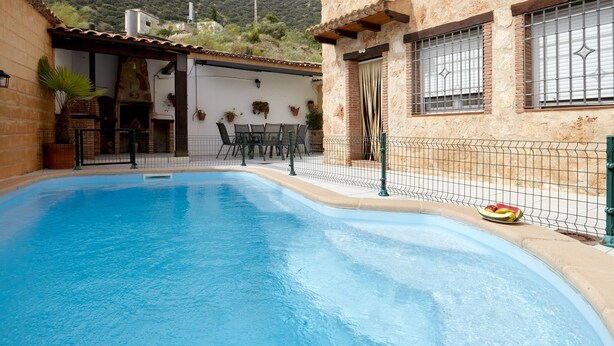 A swimming pool with a patio area, a stone building, and a mountain in the background.