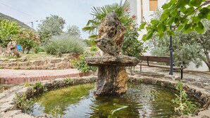 Une fontaine en pierre dans un jardin, avec un banc et différentes plantes.