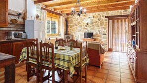 Une cuisine rustique avec des poutres en bois, des murs en pierre et un coin repas où une table est dressée pour quatre personnes.