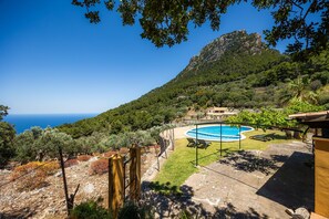 A pool with a view of the sea, surrounded by trees and a mountain.