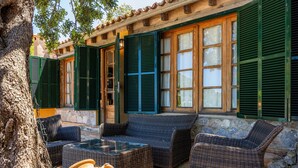 A patio area with wicker furniture, a stone wall, and green shutters. - Holiday Home 'Tramuntana' with Sea View, Private Pool and Wi-Fi (Valldemossa)