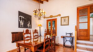 A dining area with a wooden table and chairs, a chandelier, a sewing machine, and a framed picture on the wall. - Holiday Home 'Tramuntana' with Sea View, Private Pool and Wi-Fi (Valldemossa)