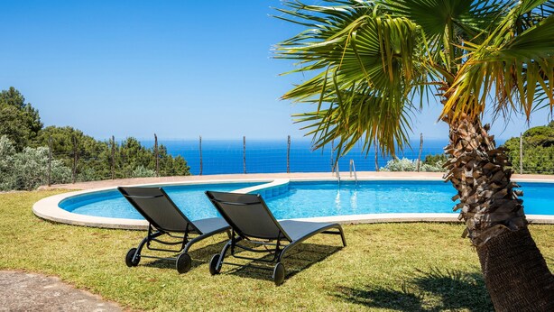 A swimming pool with two lounge chairs, a palm tree, and a view of the ocean. - Holiday Home 'Tramuntana' with Sea View, Private Pool and Wi-Fi (Valldemossa)