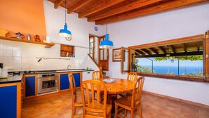 A kitchen with a dining table and chairs, wooden cabinets, and a view of the sea. - Holiday Home 'Tramuntana' with Sea View, Private Pool and Wi-Fi (Valldemossa)
