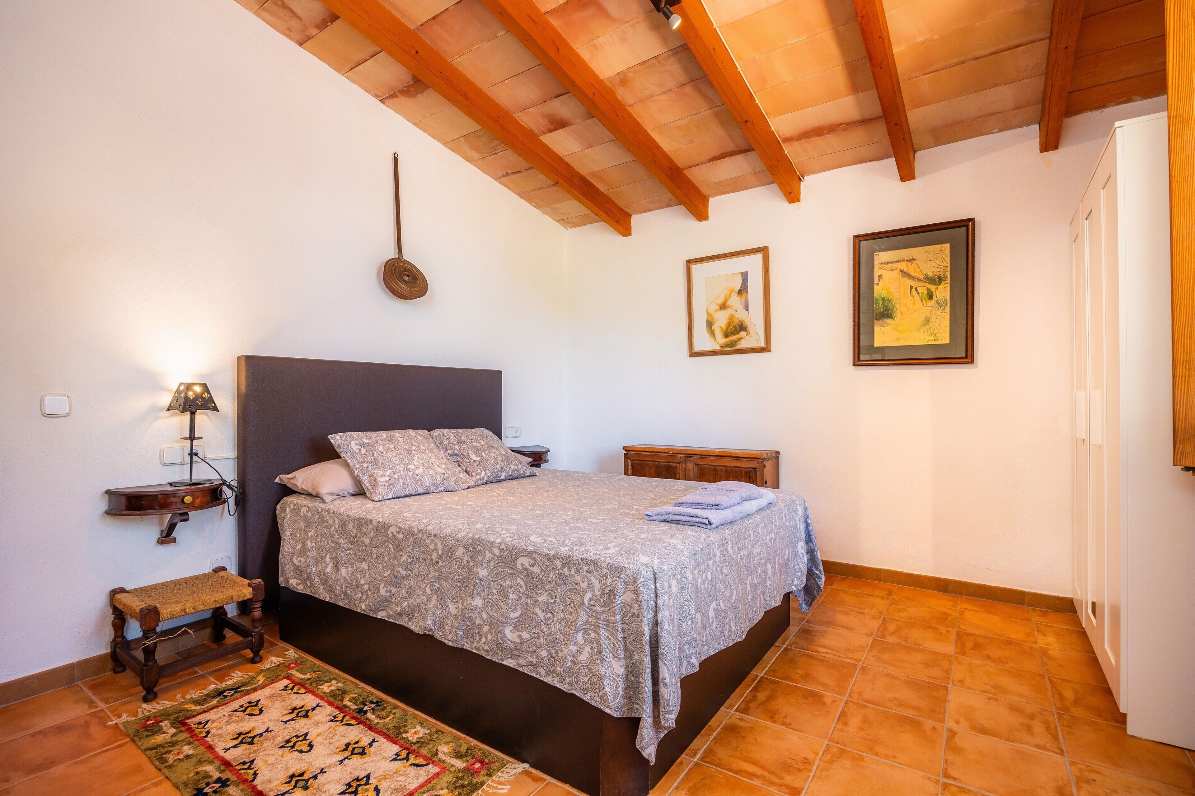 A bedroom with a bed, bedside table, lamp, and artwork on the walls.