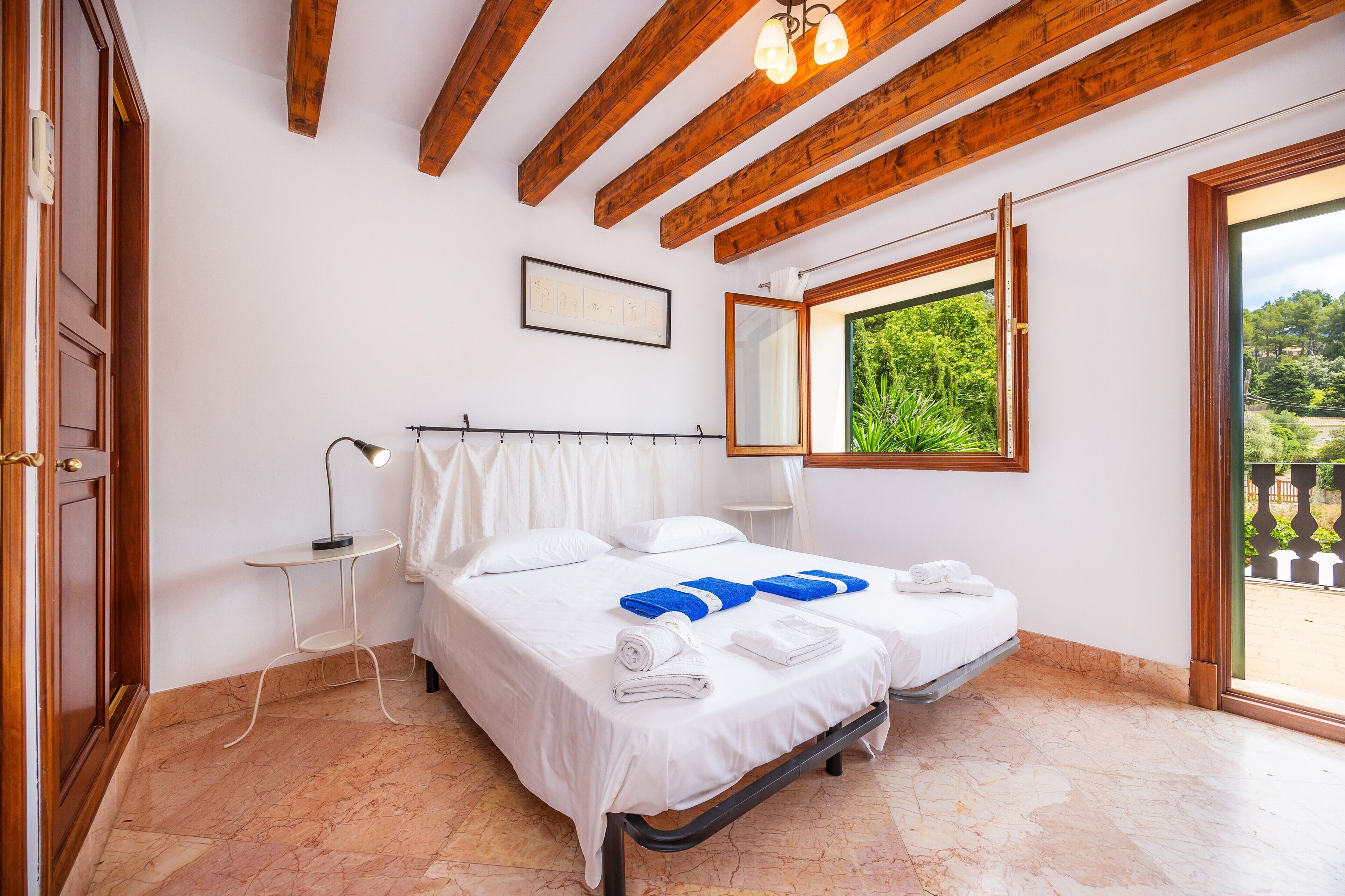 Un dormitorio con cama, mesita de noche, lámpara, ventana con vistas y vigas de madera en el techo.