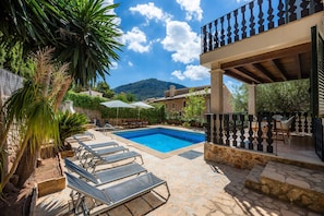 A pool area with lounge chairs, a stone patio, and a view of a mountain.