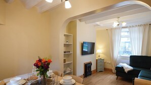 Ein Essbereich mit Tisch für vier Personen, einem an der Wand montierten Fernseher und einem Sofa im Wohnzimmer.