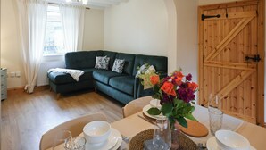 Ein gemütliches Wohnzimmer mit einem grünen Sofa, einem Esstisch mit weißen Tellern und Schüsseln sowie einer Holztür.