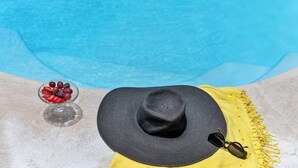 Escena junto a la piscina con un sombrero, gafas de sol y un cuenco de fruta.